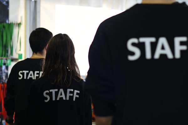 Drei Mitarbeitende in dunkler Arbeitskleidung mit STAFF-Aufdruck von hinten